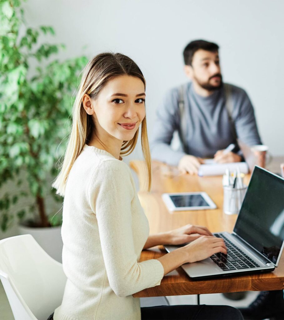 A woman at a table using a laptop. | Featured Image for the top-level Commercial Business Lawyers service landing page.